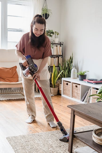 A person using their hands to load a white cloth into a yellow and black vacuum cleaner on a patterned carpet in a domestic setting. The vacuum cleaner is a portable, upright model with a flexible hos
